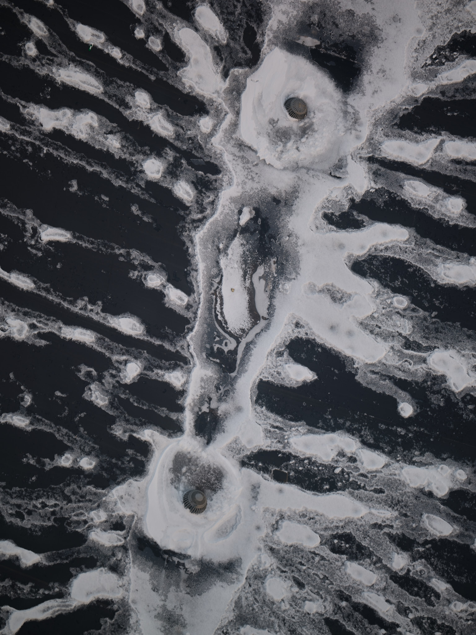 Branching snow and meltwater around two dark circular forms on a dark surface